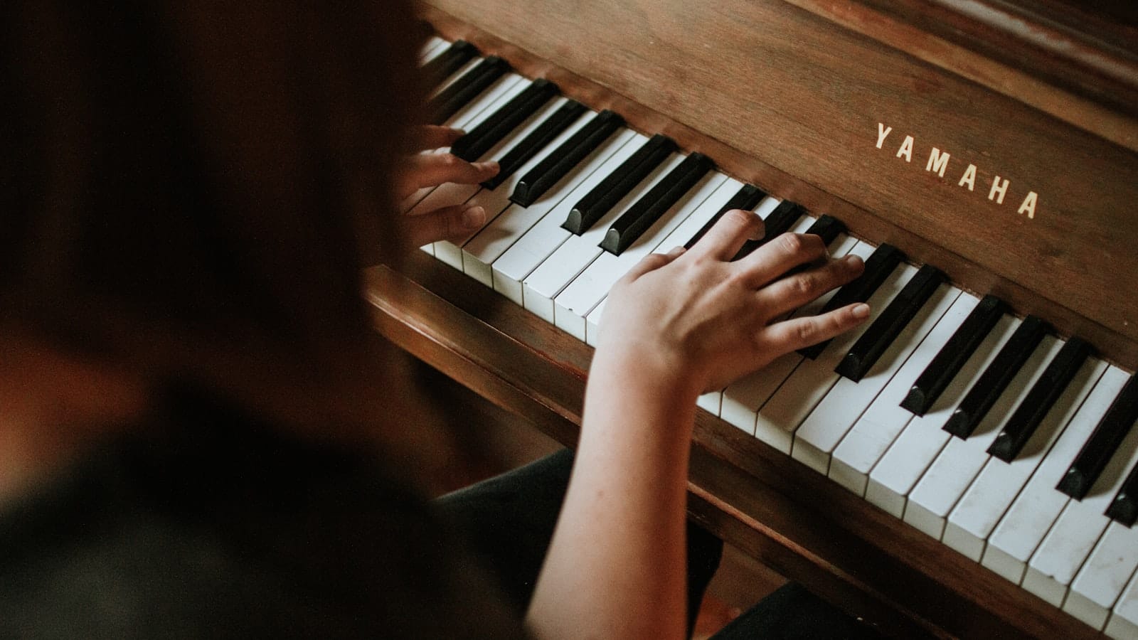 A student's hands playing an upright piano during a lesson